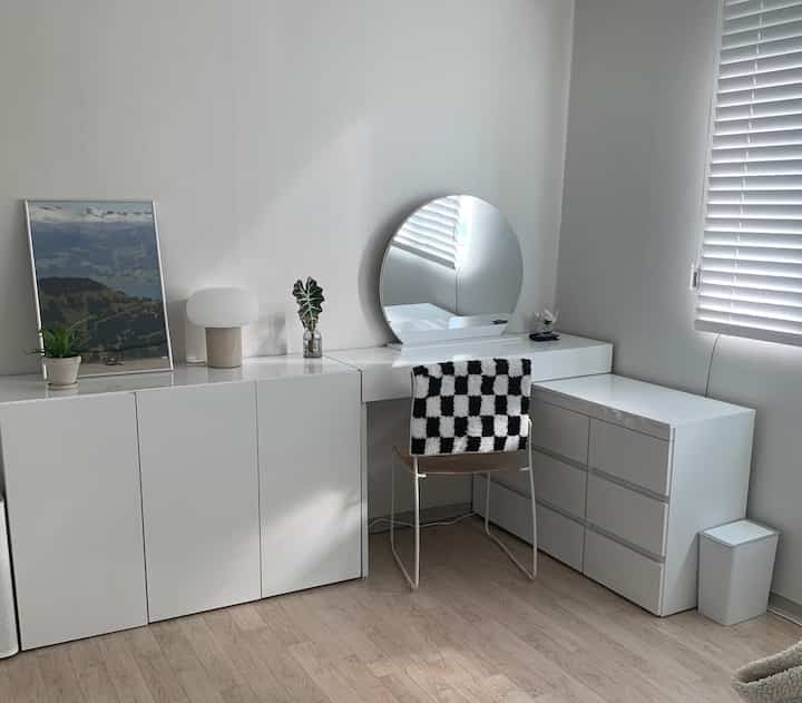 White and natural wood toned small room with vanity, dresser, and clean minimalistic modern decor