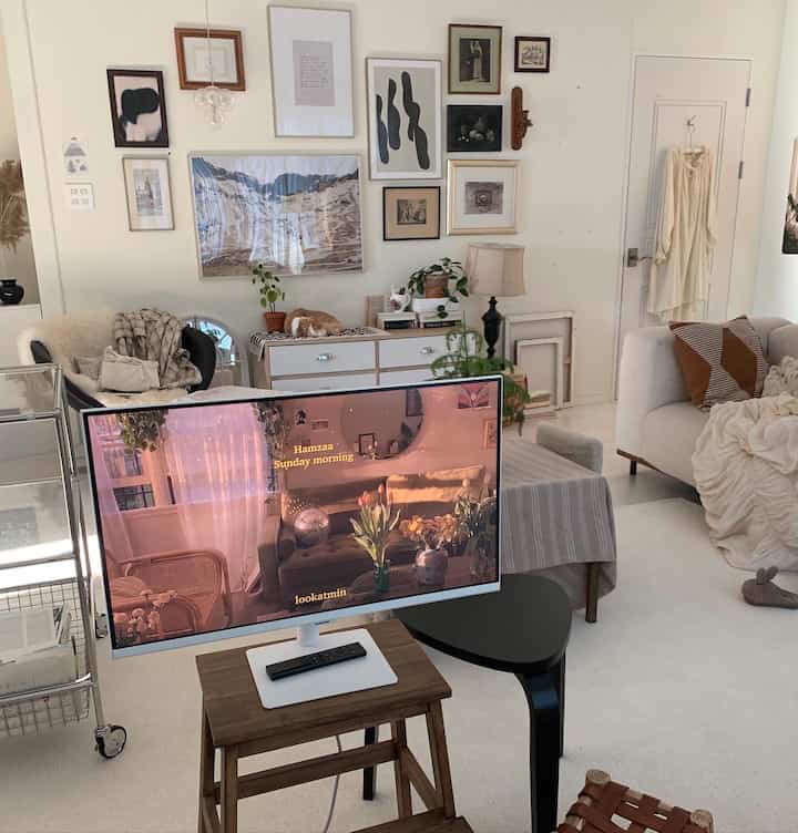 White-toned living room featuring wall art, sofa, and monitor with cozy mid-century modern style ambiance