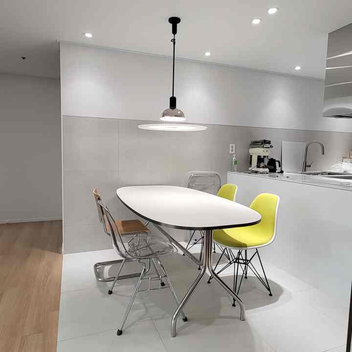 White and wood tone kitchen and dining space featuring mid-century modern furniture and transparent chairs in a clean setting