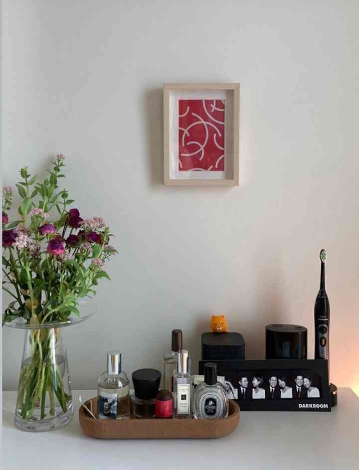 白い壁と自然な木製の額縁があるウォークインクローゼットの化粧台、香水トレイと花瓶が整然と配置されたミニマルな空間