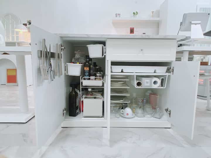 白を基調としたキッチン収納が開いており、大理石のカウンターとコーヒーカップ、皿が整頓された雰囲気のあるインテリア