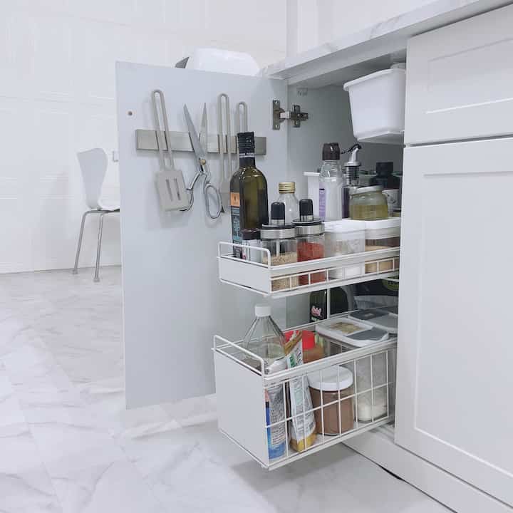 White-toned kitchen cabinet door features sliding shelves and magnetic holders neatly organizing kitchen utensils and sauce bottles