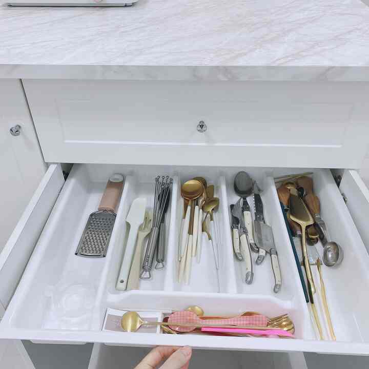 White-toned kitchen drawer interior featuring a cutlery organizer tray neatly arranged with various kitchen utensils and cutlery