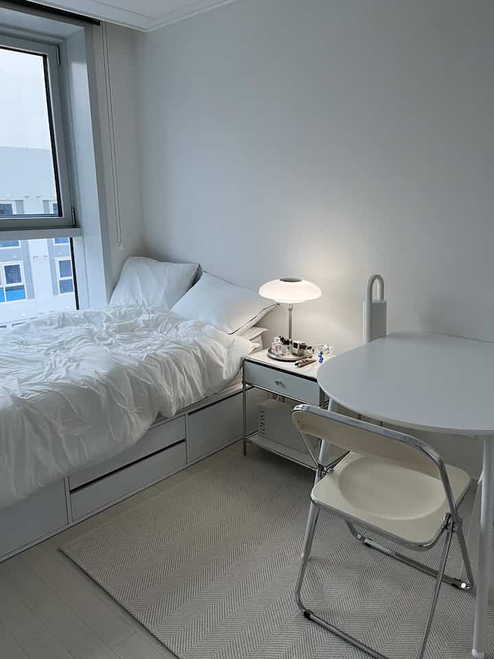 White and beige toned 6-pyeong studio apartment bedroom featuring a bed, round table, and nightstand with table lamp in a neat space