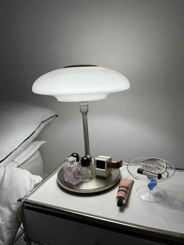 Minimal bedroom nightstand in white and gray tones featuring a modern table lamp and cosmetics