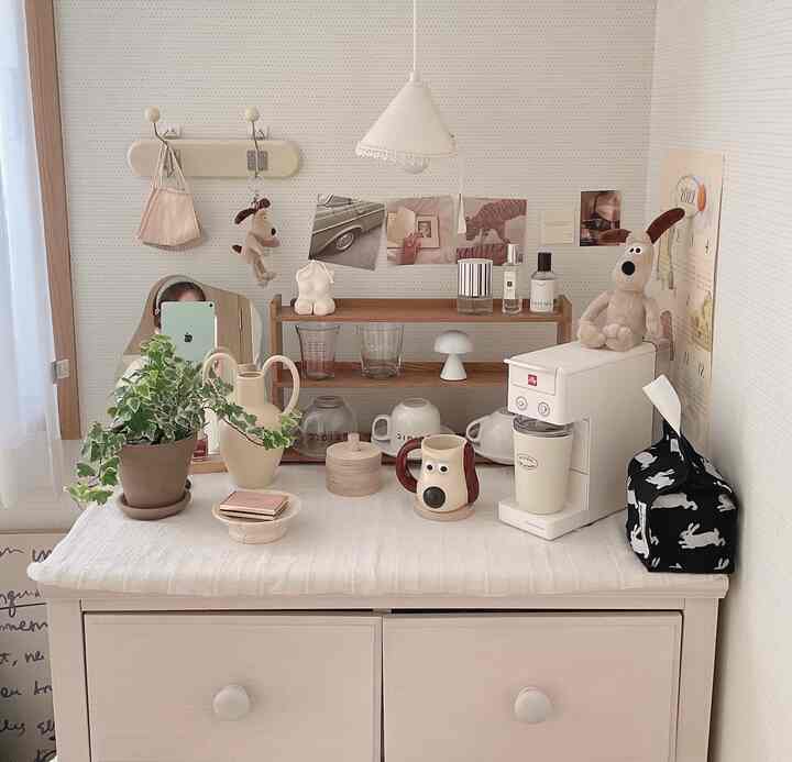 柔らかなナチュラルカラーのカフェ風空間、木製棚とイリーのコーヒーマシン、グロミットのぬいぐるみなど可愛らしい小物が配置された雰囲気のあるインテリア