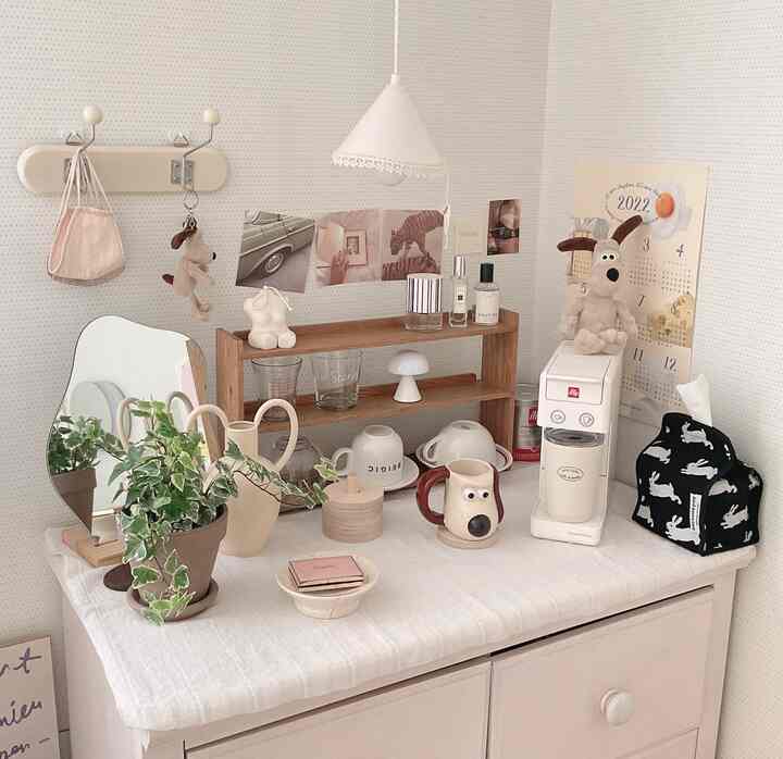 White and beige toned home cafe space featuring a coffee machine, wooden shelves, mirror, and plants creating a cozy atmosphere