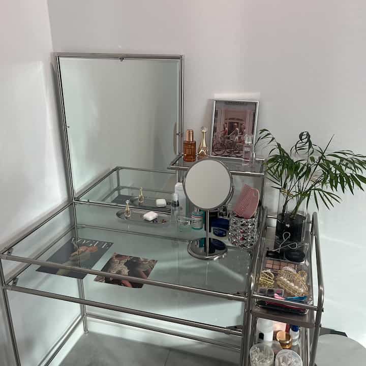 ホワイト壁に配置されたミッドセンチュリーモダン風の金属フレームとガラストップの化粧台、グリーン植物がアクセントの清潔感ある空間