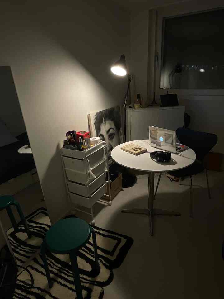 白を基調とした小さな居心地の良いワンルームのホームオフィス、丸テーブルとスツール、照明が配置された空間
