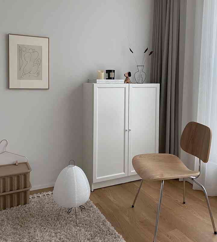 White and beige toned living room featuring a white cabinet, wooden chair, and shaggy rug, with a minimal and natural atmosphere