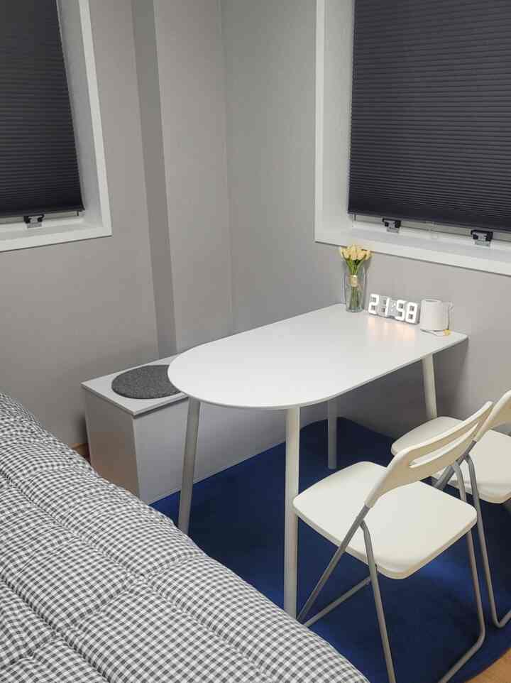 Compact bedroom in white and gray tones, featuring a white table and chairs by the window in a neat space