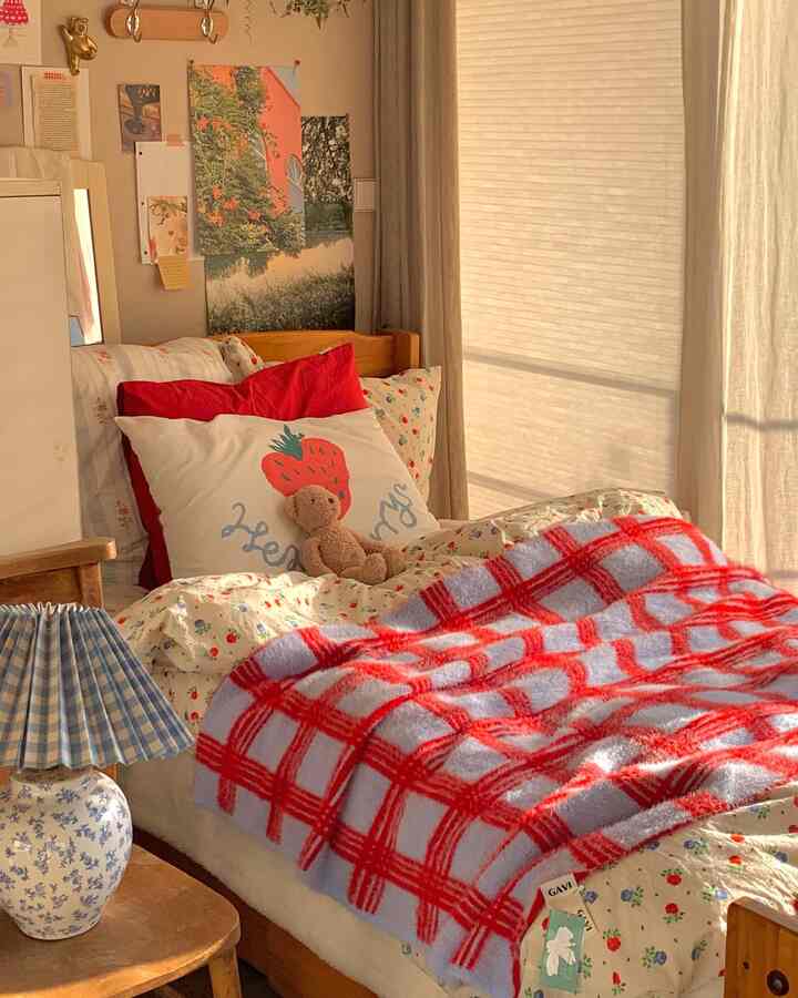 暖かいベージュ調の寝室、木製ベッドと花柄の掛け布団カバー、赤いチェックのブランケットとクッションが配置された自然な印象の空間