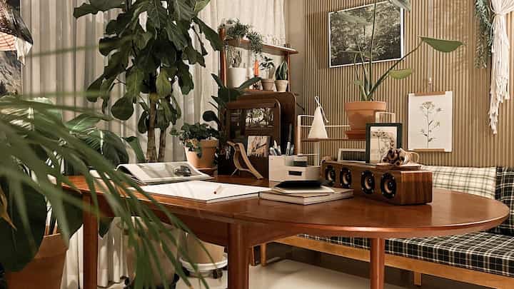 Cozy workspace with wood tones and green plants, featuring a large desk and bookshelf in a vintage style
