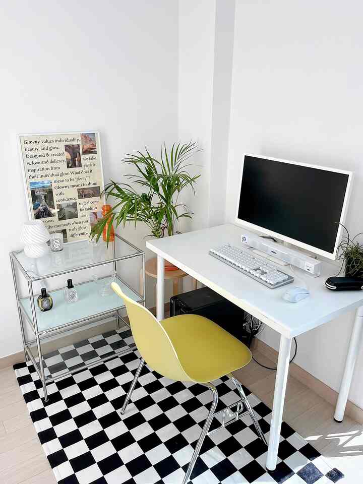 ホワイトとブラックのチェッカーボードラグが敷かれたコンパクトなホームオフィス、白いデスクとイエローのダイニングチェア、グリーンプランツが配置されたシンプルモダンなインテリア