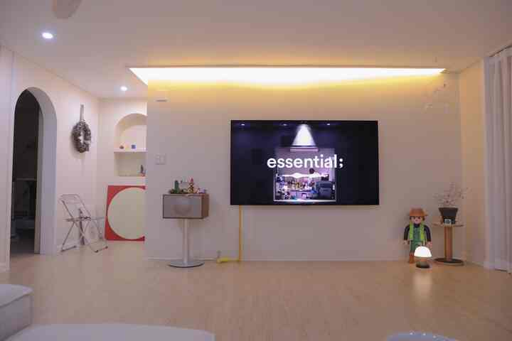 Living room with warm wood tone flooring and white walls, featuring wall-mounted TV, vintage audio, and decorative figurines in a neat setup