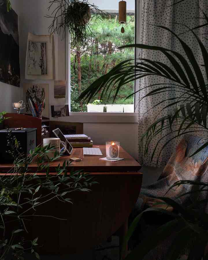 自然の景色を背景にした木製デスクと植物、カーテンが配置された温かみのあるホームオフィス