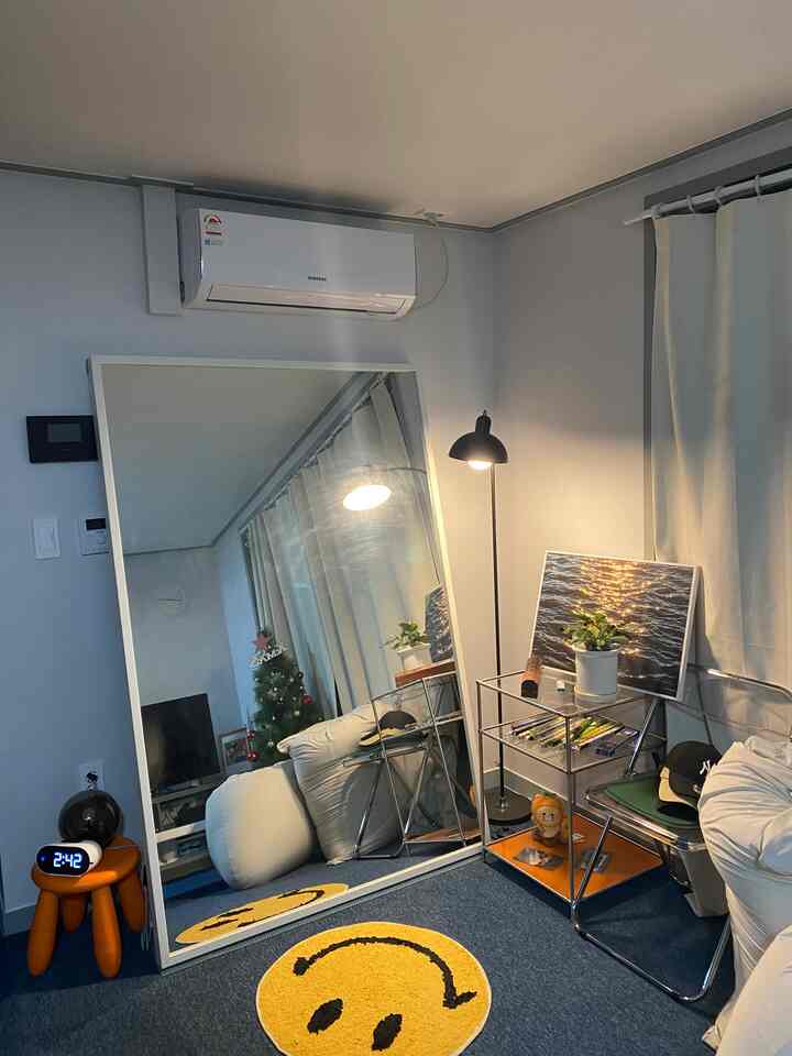 A cozy living room in white and blue tones featuring a large bean bag, smiley face rugs, big full-length mirror, and metal shelving unit