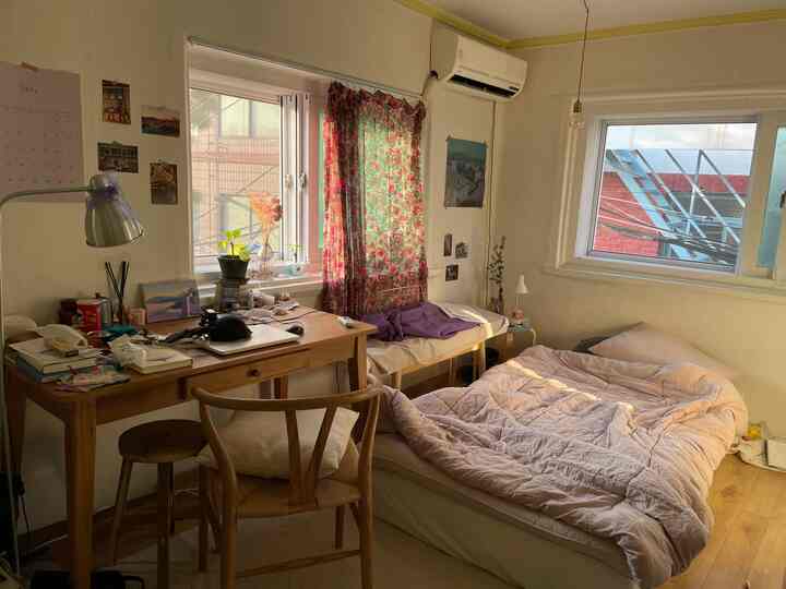 Beige and wood tone small bedroom featuring a desk, floral curtain, and warm cozy atmosphere