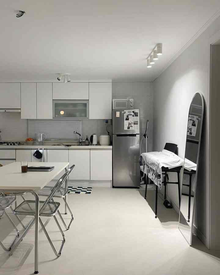 明るいホワイトトーンのキッチンスペース、ダイニングテーブルと透明な椅子、全身鏡が配置されたミニマリストなインテリア