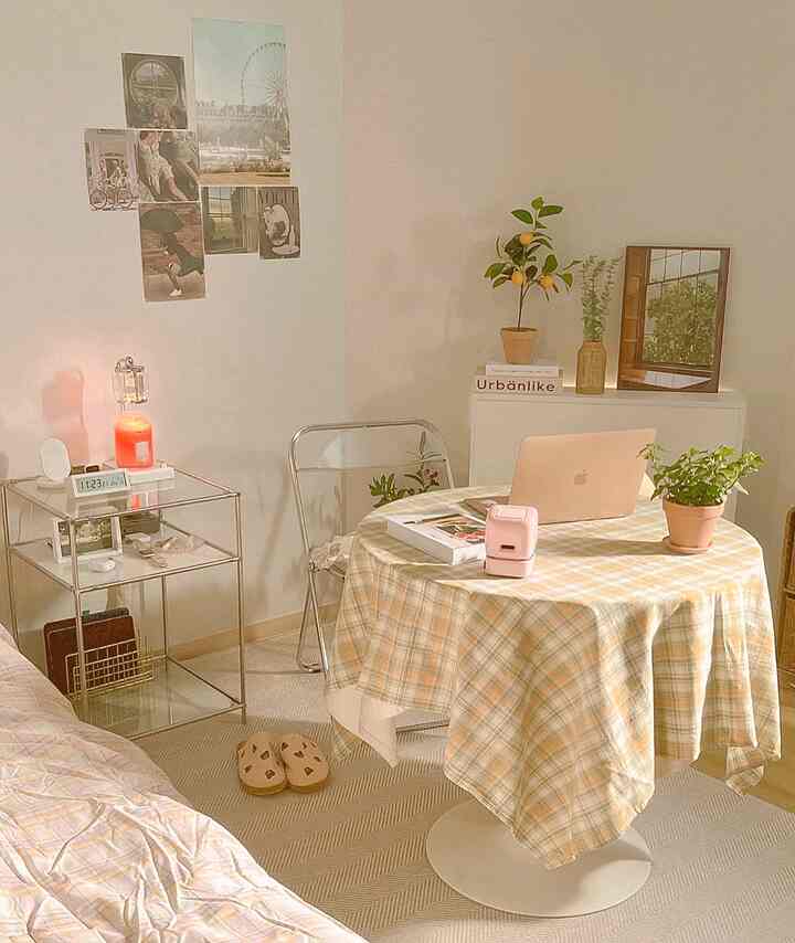 ベージュとホワイトのトーンのワンルーム、円形テーブルと透明な折り畳み椅子、植物と額縁が配置された居心地の良い暖かい一人暮らしの空間