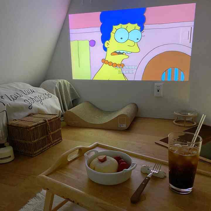 ナチュラルなトーンのワンルーム寝室、壁にプロジェクター映像、ペット用爪とぎ、木製ベッドトレイが配置された温かみのある空間