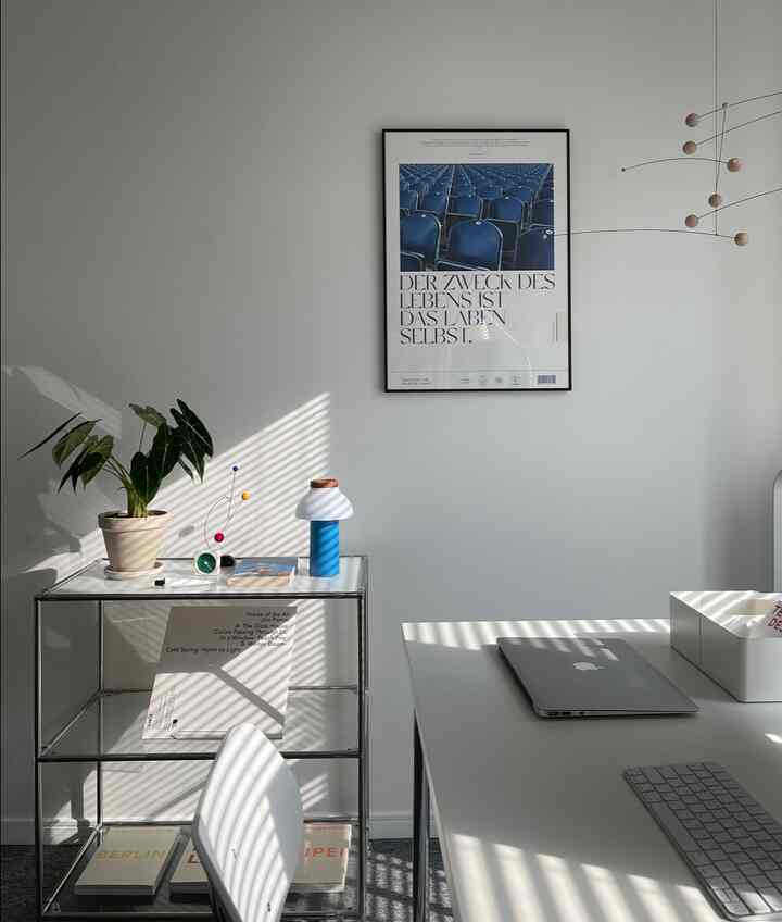White-walled mid-century modern home office with shelving and desk, featuring natural sunlight and a decorative mobile