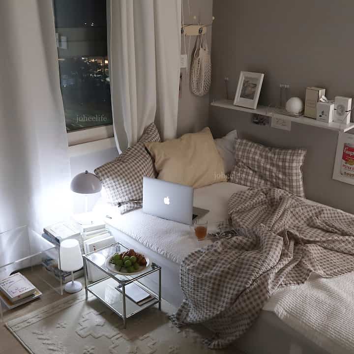 A white and beige bedroom featuring checkered bedding, a laptop, and a small tray table creating a cozy atmosphere