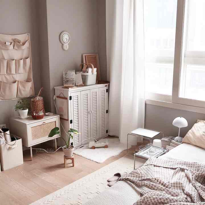 Natural beige and white toned bedroom space with compact cabinets and curtains arranged in a cozy studio apartment interior