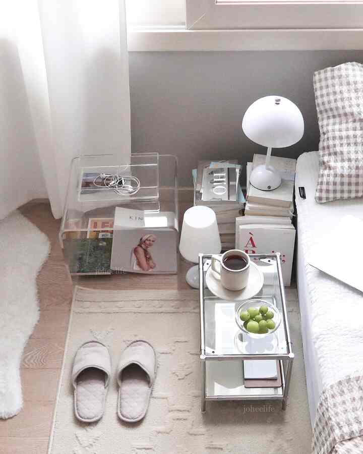 Natural color-toned compact bedroom featuring transparent acrylic side tables and cozy elements like coffee and books