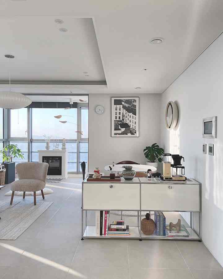 White and natural toned living room featuring mid-century modern armchair, dining table, plants, and a cozy home cafe corner with clean minimalism