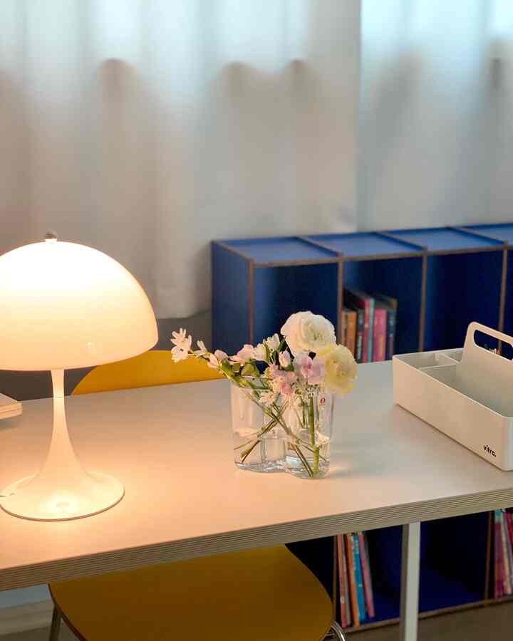 柔らかな白色調の書斎空間、白いテーブルに小さな照明と花瓶を配置したシンプルでナチュラルな雰囲気のインテリア