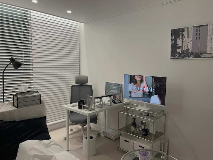 ホワイトとグレーのトーンでまとめられた狭い寝室兼ホームオフィス、デスクとオフィスチェアが配置されたシンプルなモダン空間