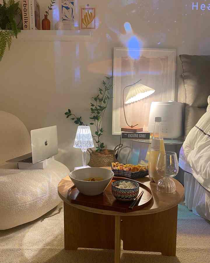 Natural modern home cafe space with white walls and natural brown wooden round table, featuring a laptop and sofa creating a cozy ambiance.