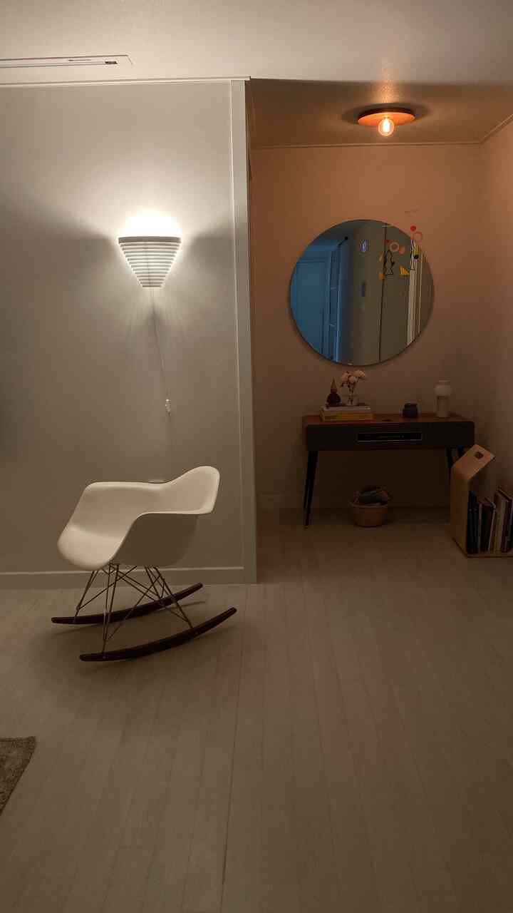 White and brown toned small entrance space featuring a white armchair and round mirror with a simple design