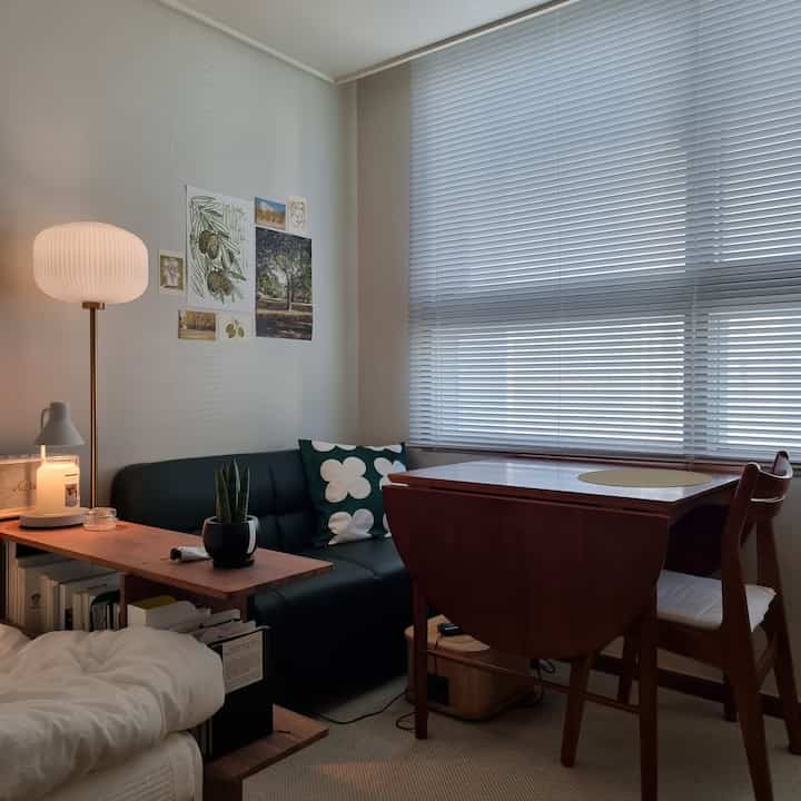 Beige-toned living room featuring black sofa and natural wood dining table with a cozy atmosphere
