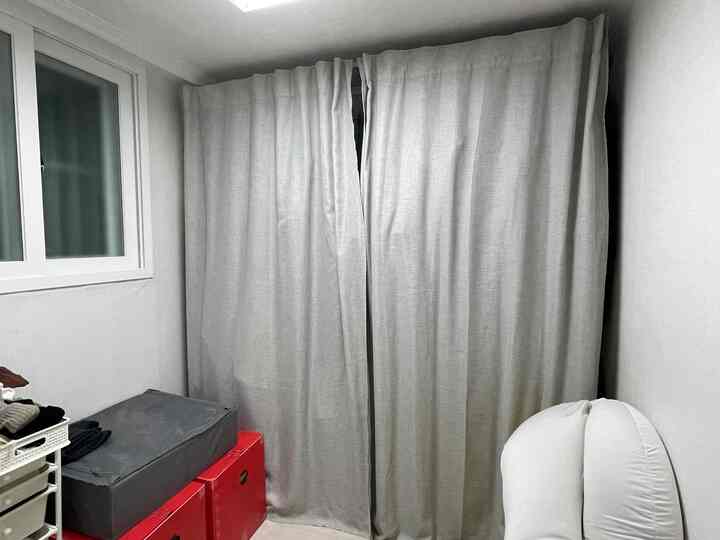 Natural-toned small closet space with gray curtains covering central area, red storage boxes and clothes folded left, and a white bean bag on the right