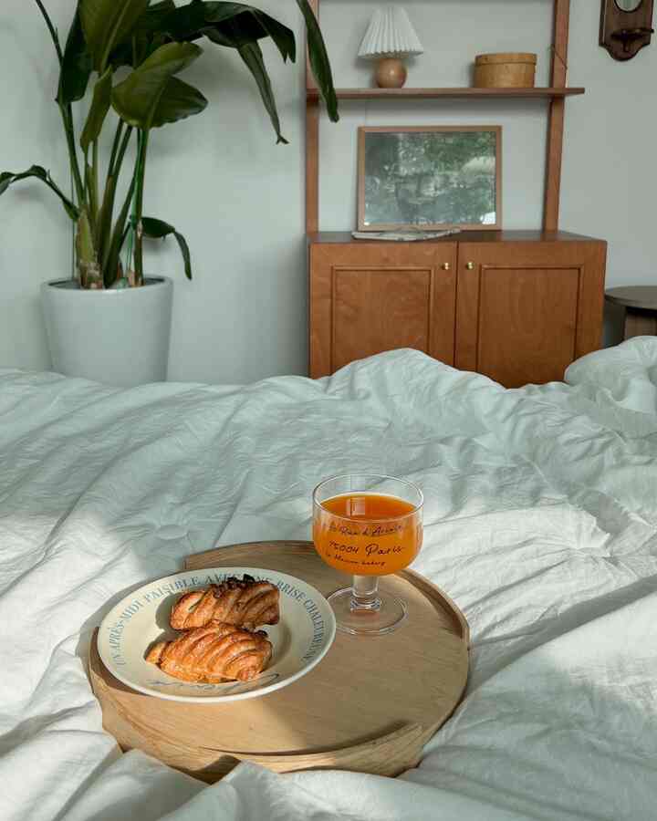 白い寝具と木目調の家具が調和するナチュラルな寝室、朝食用トレイと飲み物が置かれた雰囲気のある空間
