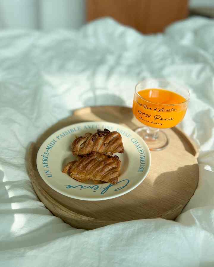 白い寝具の上に木目調のトレイが置かれ、メープルピーカンパイとオレンジジュースが配された雰囲気のある寝室の朝の風景
