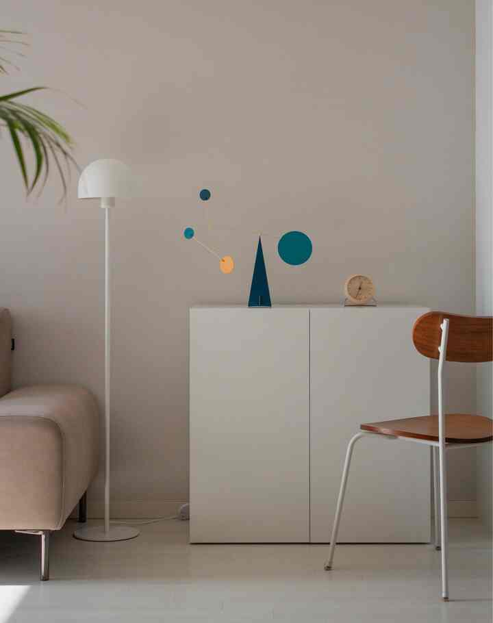 白とナチュラルカラーのリビング、白いキャビネットの上にスタンディングモビールと時計が配置されたシンプルでモダンなインテリア