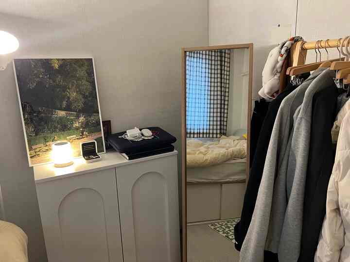 White and green toned bedroom featuring a full-length mirror, wooden clothes rack, and a storage cabinet, creating a tidy and cozy atmosphere
