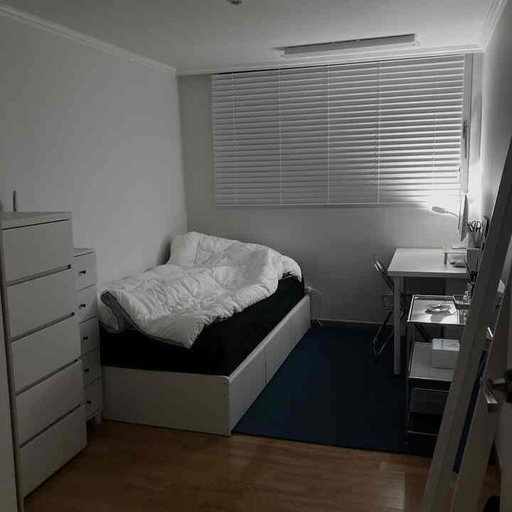 ホワイトトーンのコンパクトで狭い寝室、机とチェストが配置された実用的なインテリア