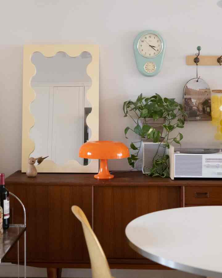 Living room with brown sideboard featuring a yellow wavy mirror and orange table lamp, creating a retro atmosphere