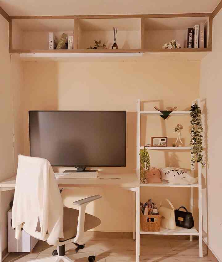 A warm home office with pale yellow walls and white furniture, featuring a computer monitor, shelves, and an office chair in a cozy workspace