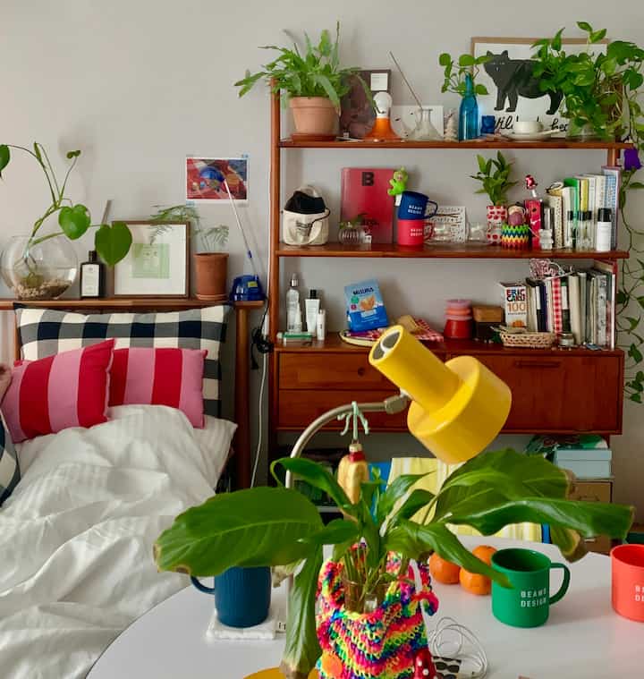 White and wood tone bedroom featuring checkered bedding, various plants, and vintage decor creating a cozy atmosphere