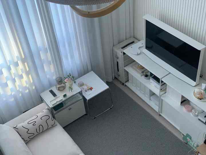 White and modern toned single household living room featuring sofa, TV stand, and curtains with a clean and simple vibe