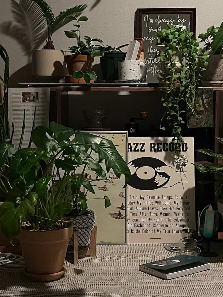 ナチュラルカラーとブラウン調のリビングルーム、多数の鉢植えとポスター、オブジェが配置された印象的なインテリア