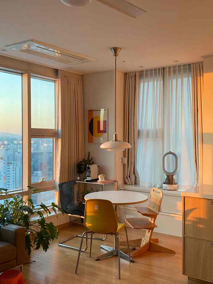 Warm beige and white toned kitchen and dining room featuring a round dining table with various chairs, curtains, and a coffee machine in a cozy setting