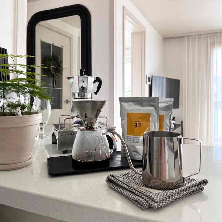 A simple home cafe setup in a white and black toned kitchen space featuring moka pot and hand drip coffee accessories