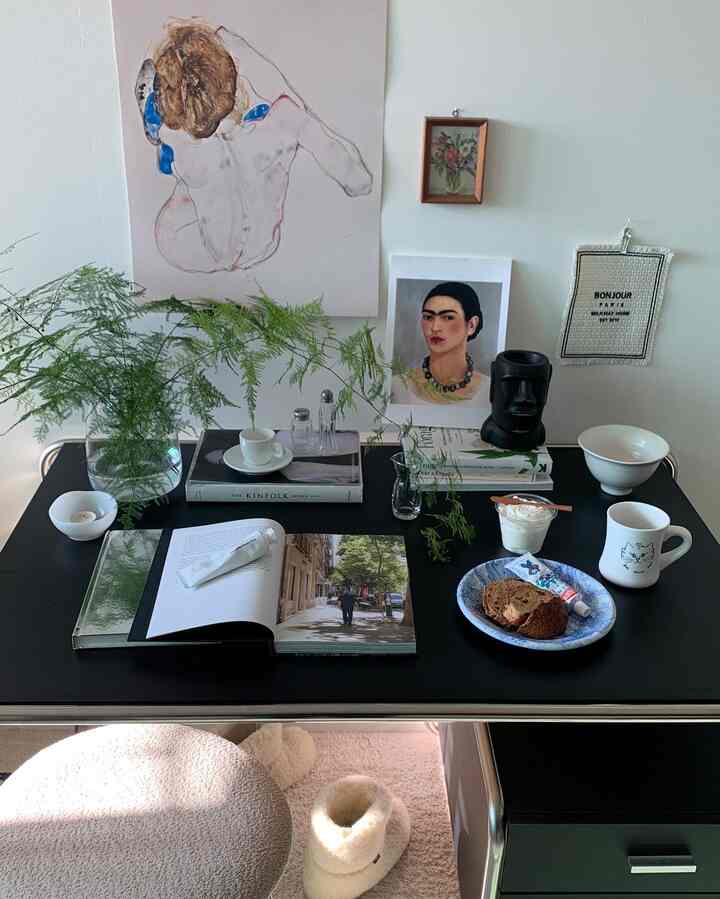 Black-toned desk featuring plant vases, art posters, and various decor items creating a cozy home cafe and workspace atmosphere