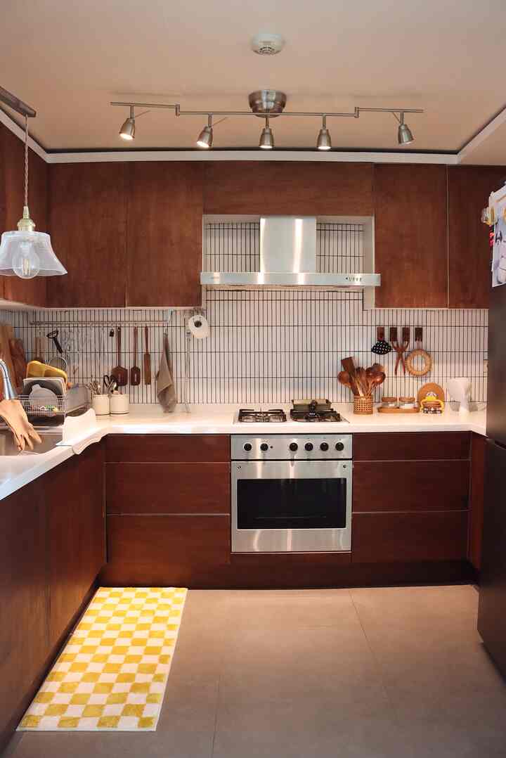 Warm brown wood and white tiled kitchen featuring kitchen utensils and ceiling spotlights for a cozy cooking space